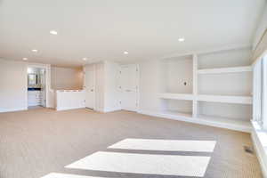 Empty room with built in features, recessed lighting, and light colored carpet