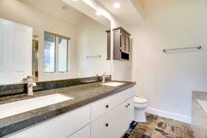 Full bath with double vanity, stone tile floors, a shower with door, and recessed lighting