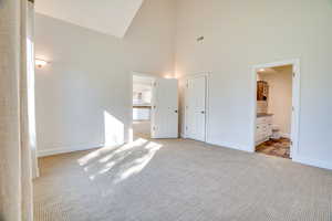 Unfurnished bedroom featuring high vaulted ceiling, light colored carpet, and ensuite bath