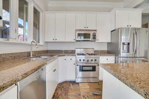 Kitchen featuring appliances with stainless steel finishes, white cabinets, dark stone finish flooring, crown molding, and light stone counters