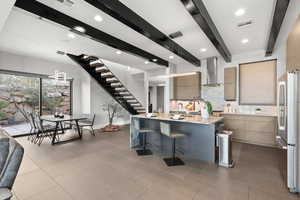 Kitchen featuring light stone countertops, modern cabinets, a kitchen bar, freestanding refrigerator, and an island with sink