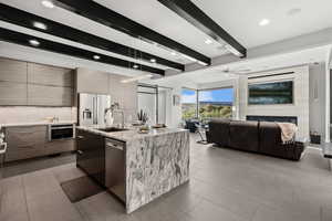 Kitchen with beam ceiling, tasteful backsplash, open floor plan, light stone counters, and a kitchen island with sink