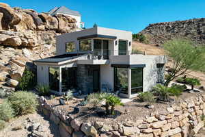 Back of property with a balcony, stucco siding, and stone siding