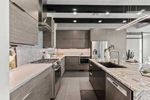 Kitchen with decorative backsplash, stainless steel appliances, light stone countertops, light tile patterned flooring, and wall chimney exhaust hood