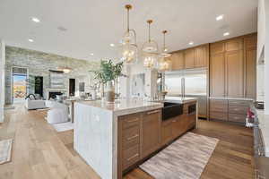 Kitchen featuring light stone counters, brown cabinetry, hanging light fixtures, built in appliances, and recessed lighting