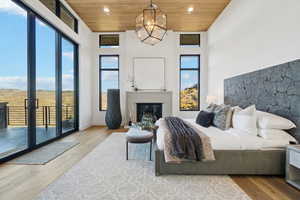Bedroom with wooden ceiling, a glass covered fireplace, wood finished floors, a chandelier, and access to exterior