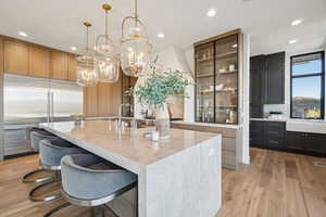 Kitchen with a breakfast bar area, a center island with sink, stainless steel built in fridge, light wood-style floors, and hanging light fixtures