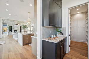 Bar with light stone countertops, light wood-style flooring, recessed lighting, pendant lighting, and a large fireplace