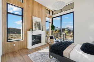 Bedroom featuring wood walls, wood finished floors, access to exterior, a glass covered fireplace, and multiple windows