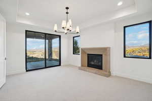 Unfurnished living room featuring a raised ceiling, light colored carpet, a tiled fireplace, recessed lighting, and a chandelier