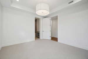 Unfurnished bedroom with a raised ceiling, carpet, ensuite bath, and recessed lighting