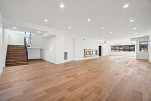 Unfurnished living room featuring recessed lighting, light wood-type flooring, and stairs
