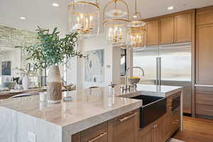 Kitchen with light stone counters, brown cabinetry, recessed lighting, and hanging light fixtures