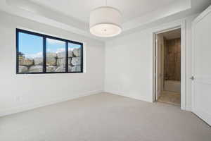 Unfurnished bedroom featuring a tray ceiling, light carpet, and ensuite bathroom