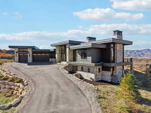 Modern home with stone siding, a chimney, asphalt driveway, and an attached garage
