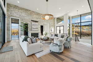 Living room featuring a wall of windows, a glass covered fireplace, light wood finished floors, recessed lighting, and a high ceiling