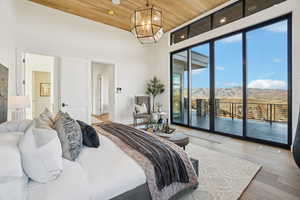 Bedroom with wood finished floors, wooden ceiling, access to outside, a mountain view, and a chandelier