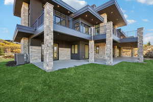 Back of property with stone siding, a lawn, a patio, and a balcony