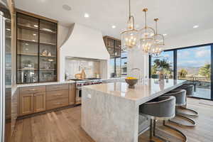 Kitchen with a kitchen bar, light stone counters, light wood-type flooring, backsplash, and recessed lighting