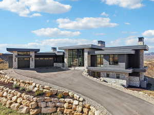 Modern home with stone siding, driveway, a garage, and a chimney