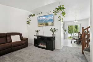 Carpeted living area featuring stairway, a glass covered fireplace, a textured ceiling, and lofted ceiling