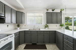 Kitchen featuring white electric stove, healthy amount of natural light, a textured ceiling, gray cabinetry, and light countertops