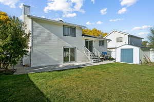 Back of house with a patio, a storage unit, a lawn, and a chimney