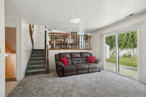 Living area with stairs, a textured ceiling, and carpet floors