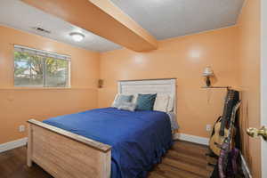 Bedroom with a textured ceiling, dark wood-style flooring, and beamed ceiling