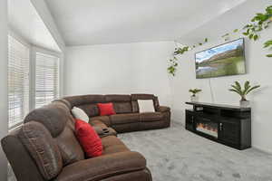 Carpeted living area with lofted ceiling, a glass covered fireplace, and a textured ceiling