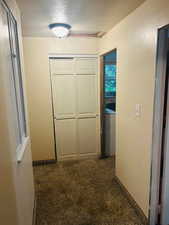 Hall featuring a textured ceiling and dark carpet