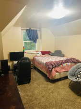 Bedroom with a textured ceiling, carpet flooring, and lofted ceiling