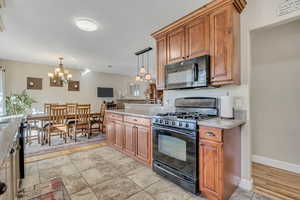 Kitchen with black appliances, brown cabinets, pendant lighting, and light stone counters