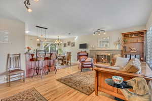 Living area featuring rail lighting, light wood finished floors, a stone fireplace, and a chandelier
