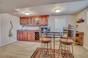 Basement Apartment Kitchen featuring glass insert cabinets, light carpet, light countertops, brown cabinetry, and a textured ceiling