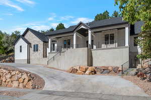 View of front of house featuring stone siding, board and batten siding, stairs, and covered porch