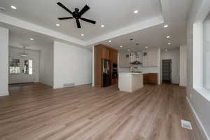 Kitchen featuring open floor plan, a center island with sink, a raised ceiling, and recessed lighting