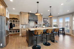 Kitchen featuring backsplash, light wood-type flooring, pendant lighting, a kitchen breakfast bar, and stainless steel fridge with ice dispenser