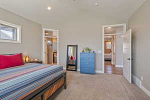 Carpeted bedroom with multiple windows, vaulted ceiling, ensuite bath, and recessed lighting