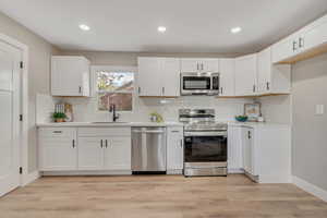 Kitchen featuring appliances with stainless steel finishes, white cabinetry, backsplash, recessed lighting, and light wood finished floors