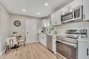 Kitchen with appliances with stainless steel finishes, decorative backsplash, white cabinetry, light wood finished floors, and recessed lighting