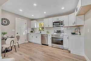 Kitchen with stainless steel appliances, white cabinetry, tasteful backsplash, recessed lighting, and light wood finished floors