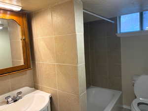 Bathroom with bathtub / shower combination, vanity, a textured ceiling, and tile walls