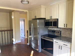 Kitchen featuring appliances with stainless steel finishes, dark wood-style flooring, tasteful backsplash, granite counters, and white cabinetry