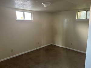 Basement featuring a textured ceiling, healthy amount of natural light, and dark colored carpet