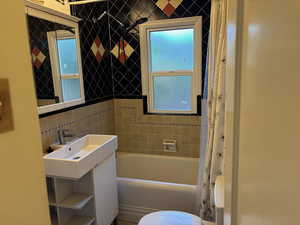 Full bathroom with shower / tub combo with curtain, vanity, tasteful backsplash, and tile walls