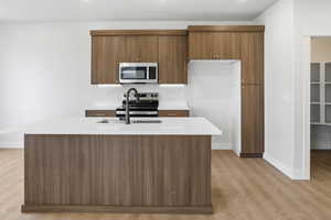 Kitchen featuring brown cabinets, appliances with stainless steel finishes, light wood-style floors, a kitchen island with sink, and modern cabinets