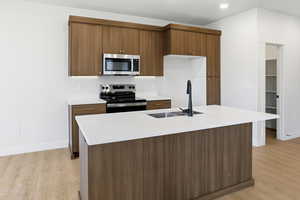 Kitchen featuring modern cabinets, stainless steel appliances, a center island with sink, and brown cabinets