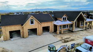 Property under construction featuring a mountain view, covered porch, a garage, driveway, and a shingled roof