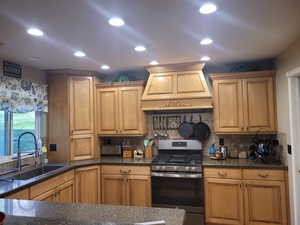Kitchen with stainless steel gas range, custom exhaust hood, recessed lighting, tasteful backsplash, and dark stone counters